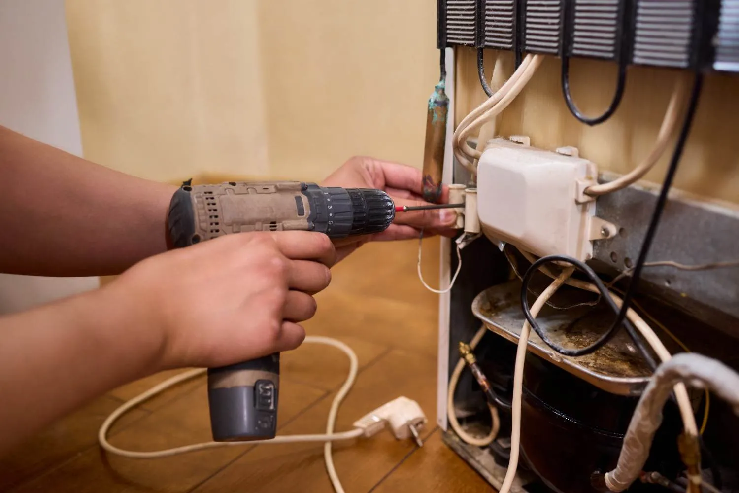 Technician using a drill on the wiring behind a refrigerator